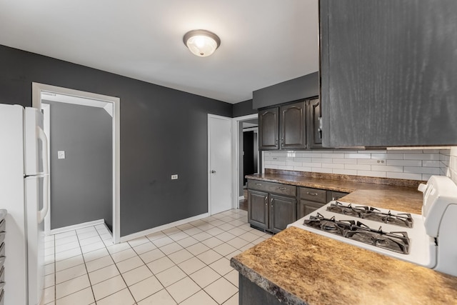 kitchen with tasteful backsplash, stovetop, white refrigerator, light tile patterned floors, and dark brown cabinets