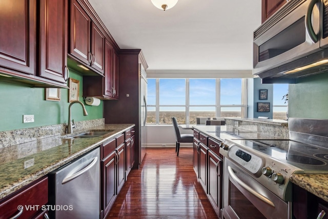 kitchen with light stone countertops, sink, stainless steel appliances, and dark wood-type flooring