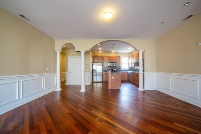 kitchen featuring decorative columns, appliances with stainless steel finishes, tasteful backsplash, dark wood-type flooring, and a center island