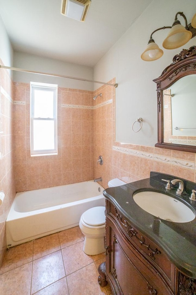 full bathroom featuring toilet, vanity, tile walls, tiled shower / bath, and tile patterned floors