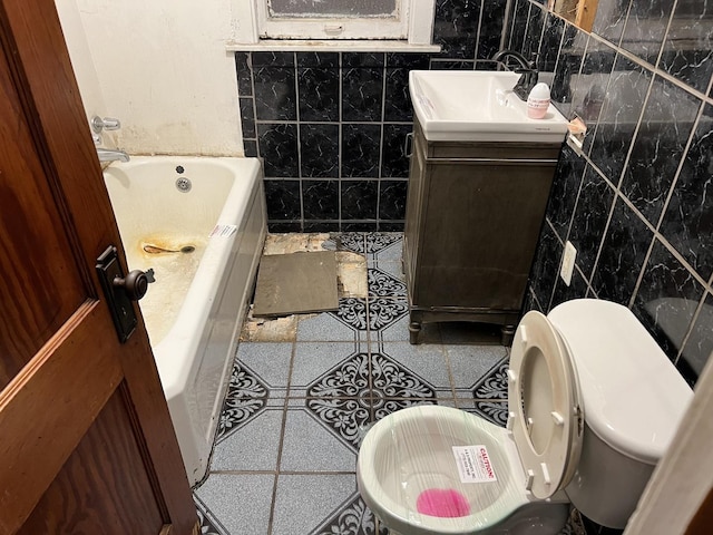 bathroom featuring toilet, vanity, tile walls, tile patterned floors, and a tub