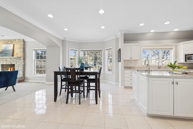 dining space with sink, a stone fireplace, ornamental molding, and light tile patterned flooring