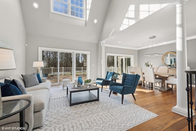 living room featuring decorative columns, crown molding, a high ceiling, and light hardwood / wood-style flooring