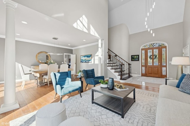 living room featuring decorative columns, crown molding, a high ceiling, and light hardwood / wood-style flooring