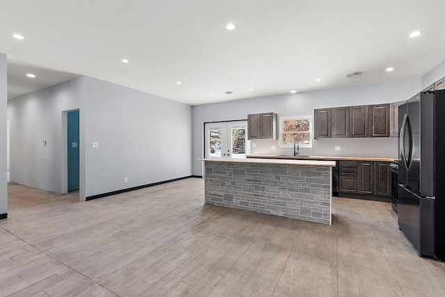 kitchen with dark brown cabinetry, visible vents, freestanding refrigerator, light wood-type flooring, and a sink