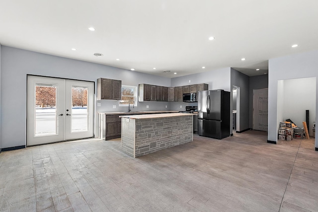 kitchen featuring a center island, light countertops, stainless steel microwave, freestanding refrigerator, and dark brown cabinets