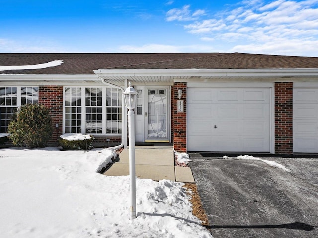 snow covered property entrance featuring a shingled roof and brick siding