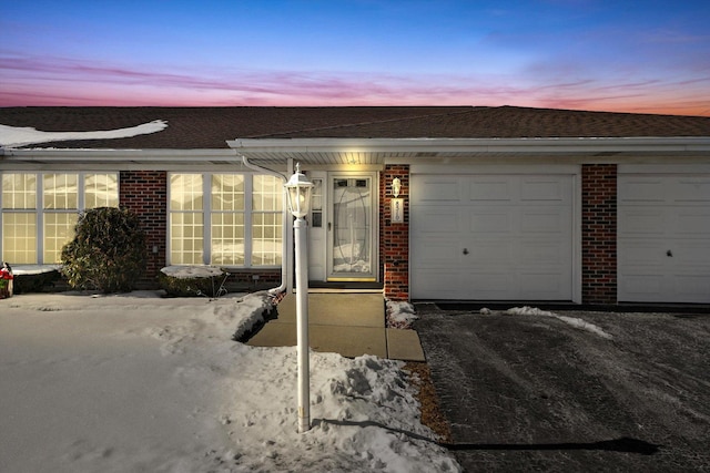 view of front of property featuring brick siding, driveway, an attached garage, and roof with shingles