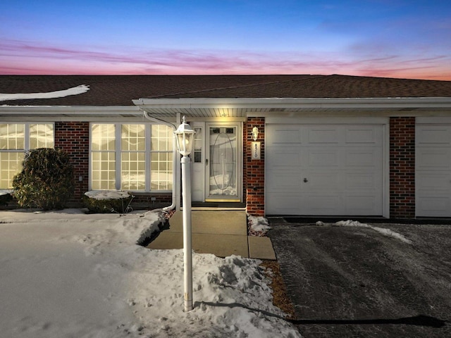 doorway to property featuring a garage, driveway, and brick siding