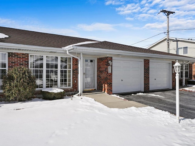 ranch-style home featuring brick siding, an attached garage, a shingled roof, and aphalt driveway