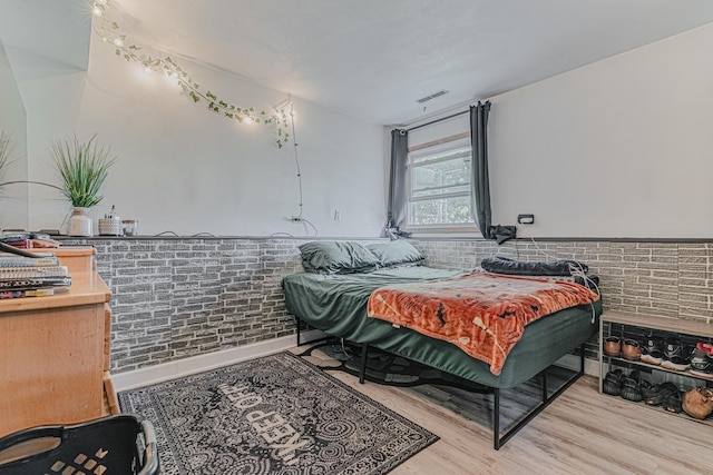 bedroom with brick wall and light hardwood / wood-style floors