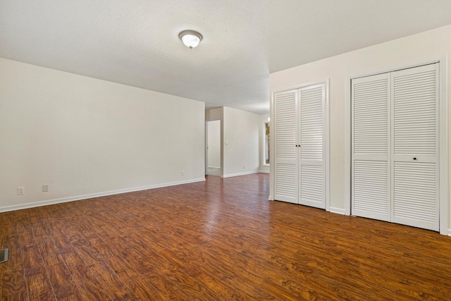 unfurnished bedroom with dark hardwood / wood-style flooring and two closets