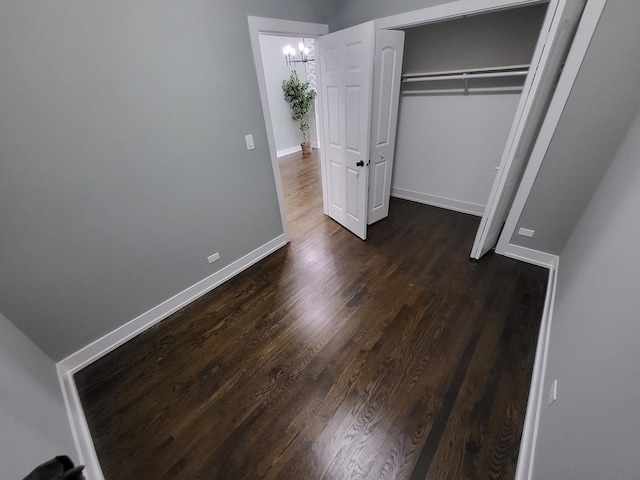 unfurnished bedroom with a chandelier, a closet, dark wood finished floors, and baseboards