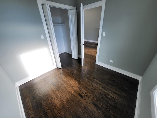 unfurnished bedroom featuring baseboards, dark wood finished floors, and a closet