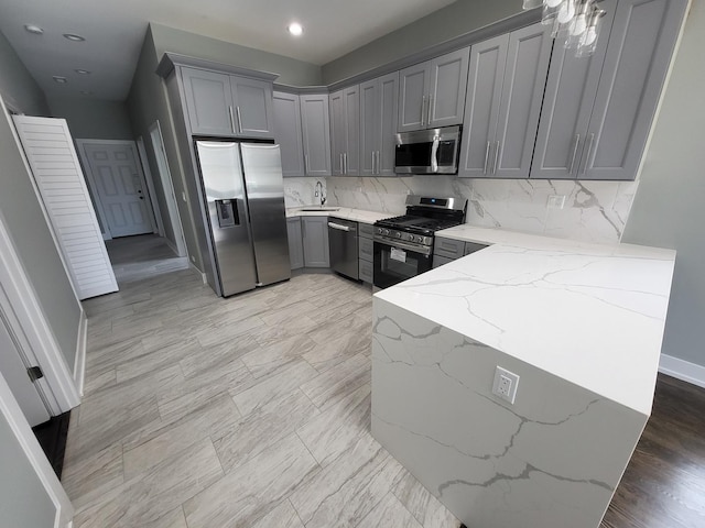 kitchen featuring light stone countertops, gray cabinetry, stainless steel appliances, a sink, and decorative backsplash