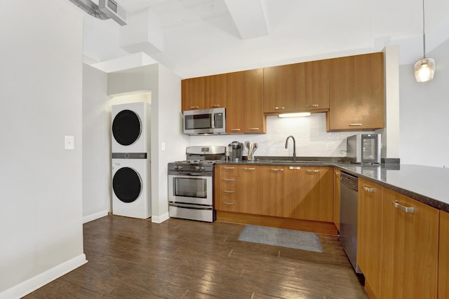 kitchen with stacked washer and clothes dryer, stainless steel appliances, dark hardwood / wood-style flooring, pendant lighting, and sink