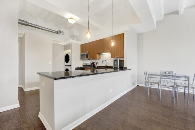 kitchen featuring decorative light fixtures, kitchen peninsula, sink, stacked washer / dryer, and stainless steel appliances