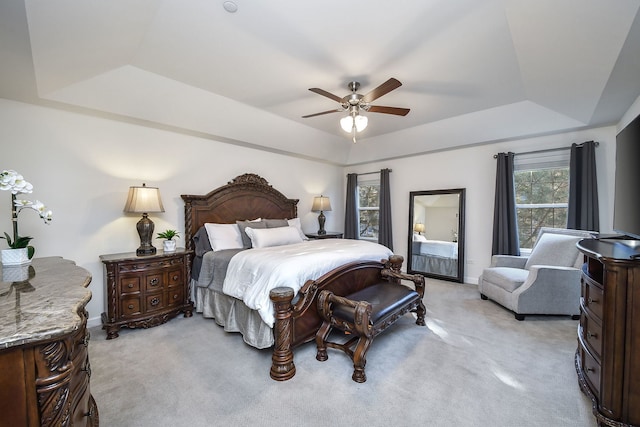 bedroom with ceiling fan, light colored carpet, and a tray ceiling