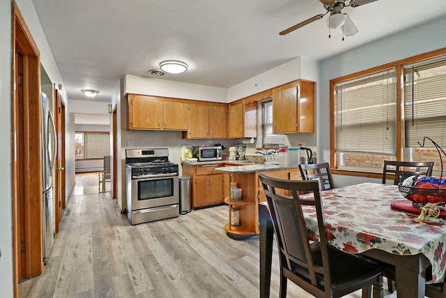 kitchen with appliances with stainless steel finishes, kitchen peninsula, ceiling fan, light hardwood / wood-style floors, and backsplash