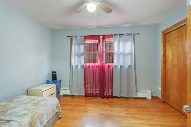 bedroom with ceiling fan, a baseboard radiator, light hardwood / wood-style floors, and a closet