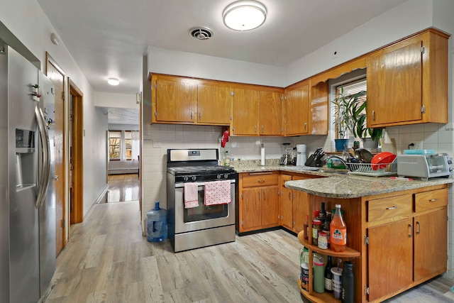 kitchen with backsplash, a baseboard heating unit, light hardwood / wood-style floors, stainless steel appliances, and light stone countertops