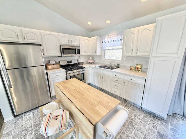 kitchen featuring white cabinetry, appliances with stainless steel finishes, backsplash, vaulted ceiling, and sink