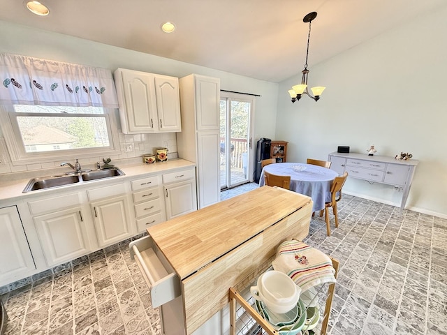 kitchen featuring decorative backsplash, sink, white cabinetry, hanging light fixtures, and a chandelier