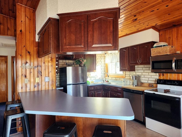 kitchen featuring a breakfast bar, kitchen peninsula, sink, appliances with stainless steel finishes, and wooden ceiling