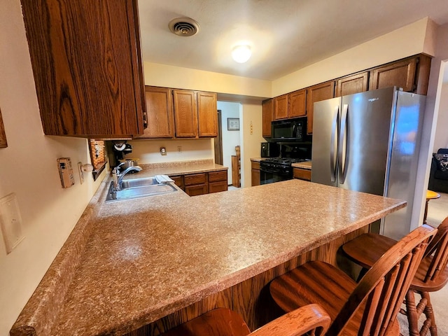 kitchen featuring kitchen peninsula, a kitchen breakfast bar, stainless steel refrigerator, range with gas stovetop, and sink