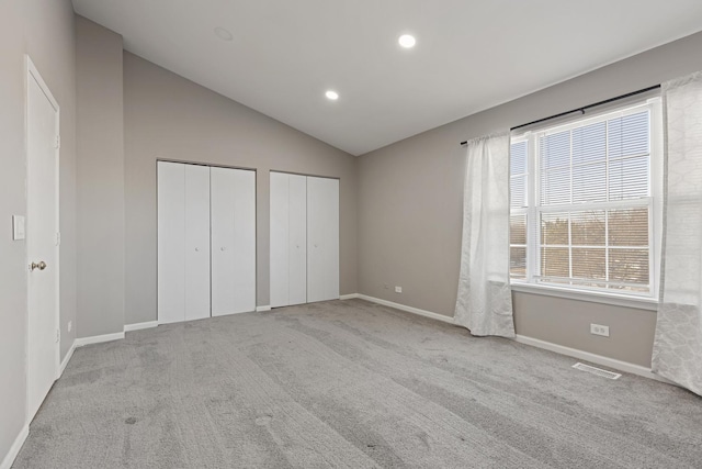 unfurnished bedroom with two closets, light carpet, and lofted ceiling