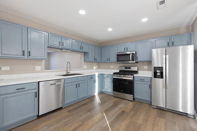 kitchen with hardwood / wood-style flooring, stainless steel appliances, blue cabinetry, light stone counters, and sink