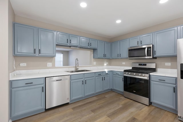 kitchen featuring blue cabinets, sink, stainless steel appliances, and light hardwood / wood-style flooring