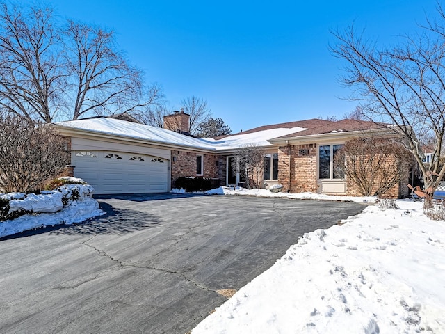 ranch-style house with brick siding, driveway, a chimney, and an attached garage