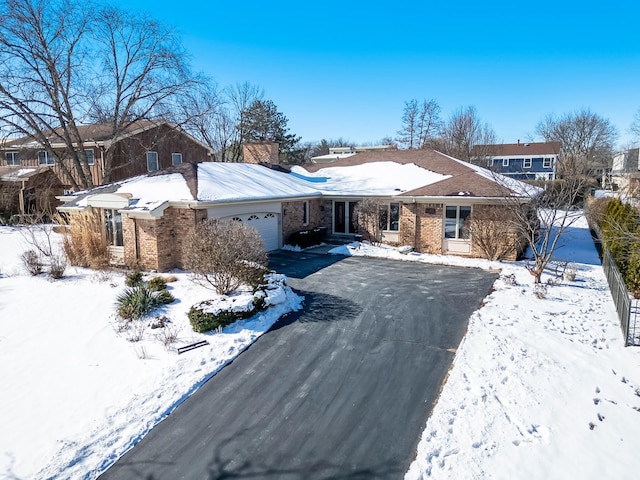 ranch-style home featuring a garage, a chimney, aphalt driveway, and brick siding