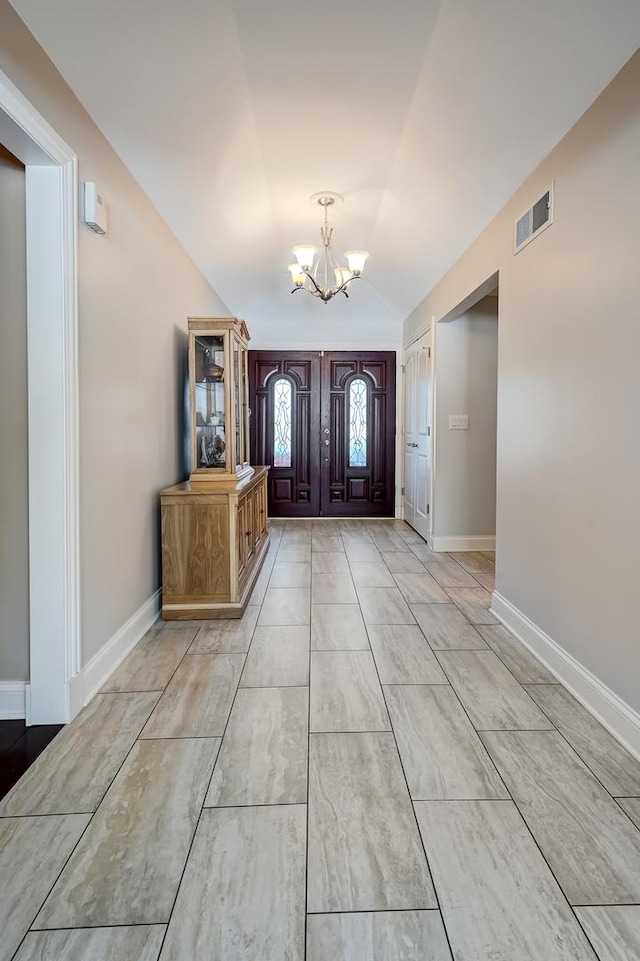 foyer entrance with baseboards, vaulted ceiling, visible vents, and a chandelier