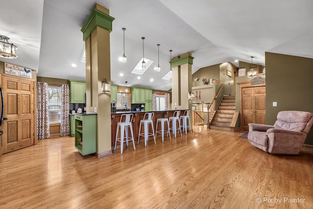 kitchen with light hardwood / wood-style floors, kitchen peninsula, green cabinets, a kitchen breakfast bar, and vaulted ceiling