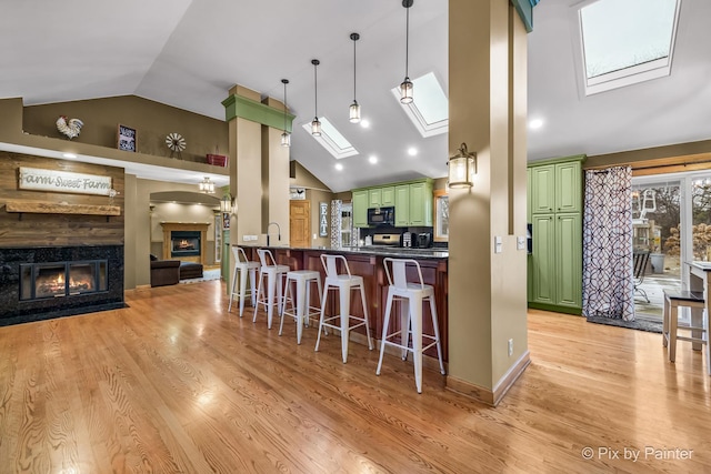 kitchen featuring kitchen peninsula, a skylight, a kitchen breakfast bar, green cabinetry, and a high end fireplace