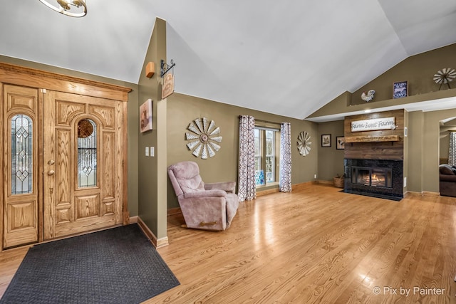 entrance foyer with vaulted ceiling, a large fireplace, and light hardwood / wood-style flooring