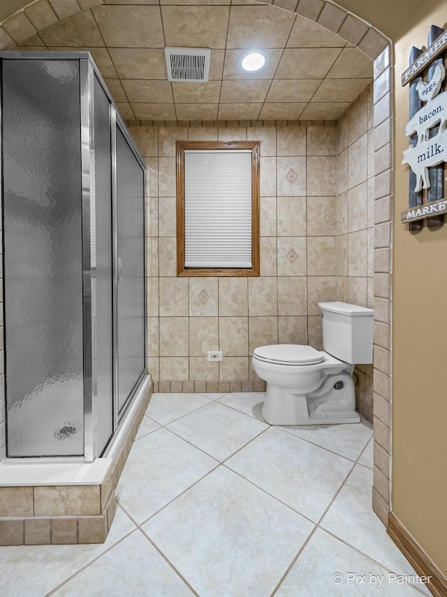 bathroom with toilet, tile walls, tile patterned floors, and a shower with door