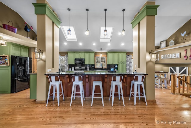 kitchen with black appliances, decorative backsplash, kitchen peninsula, light wood-type flooring, and green cabinets