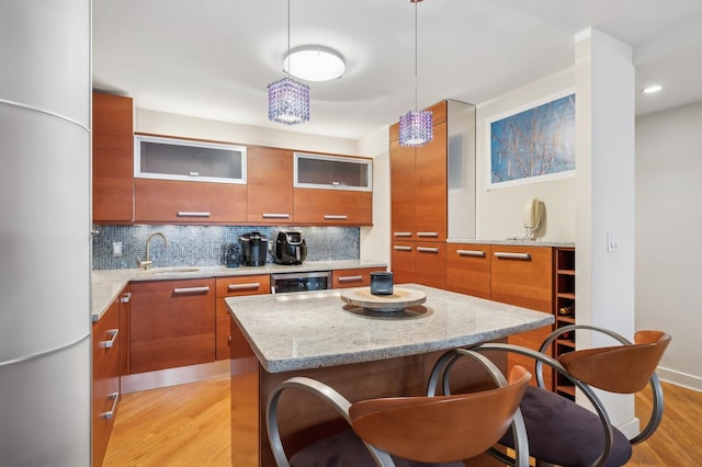 kitchen with sink, a center island, hanging light fixtures, light wood-type flooring, and backsplash