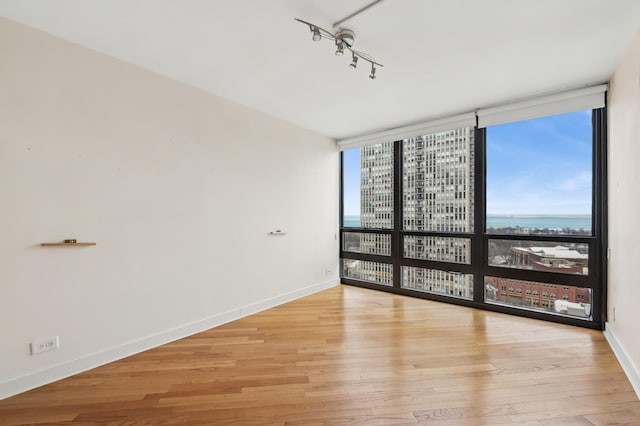 spare room with expansive windows, a water view, and light hardwood / wood-style floors