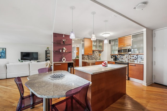 kitchen with pendant lighting, appliances with stainless steel finishes, a kitchen breakfast bar, a center island, and tasteful backsplash