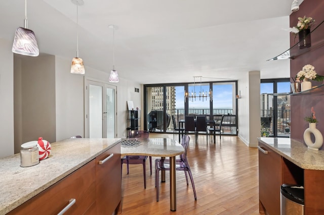 kitchen featuring decorative light fixtures, a wall of windows, light hardwood / wood-style floors, light stone countertops, and french doors