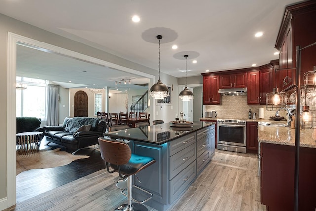 kitchen featuring decorative light fixtures, light wood-type flooring, dark stone counters, stainless steel stove, and sink