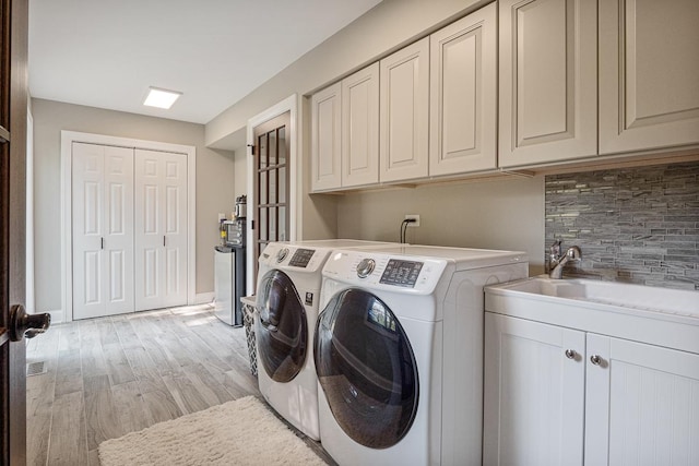 laundry area with sink, washer and dryer, light hardwood / wood-style floors, and cabinets