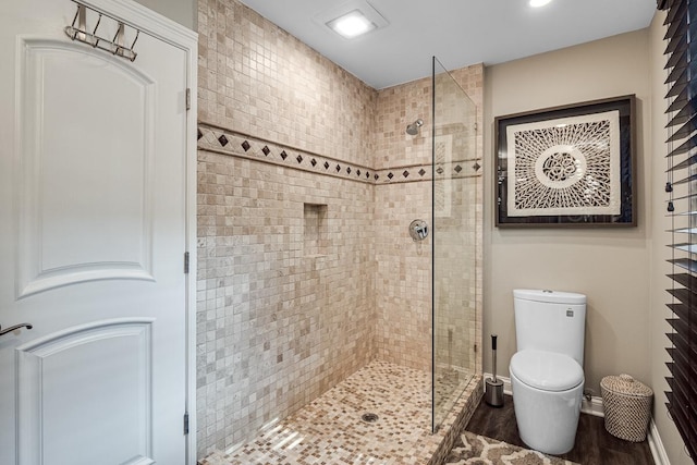 bathroom with wood-type flooring, toilet, and a tile shower