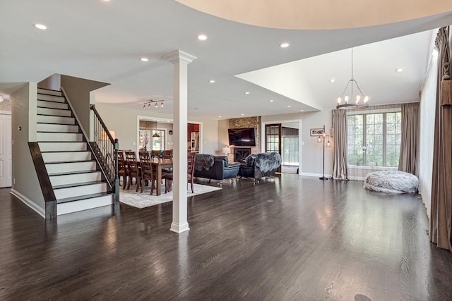 living room with an inviting chandelier, a large fireplace, dark hardwood / wood-style flooring, and decorative columns