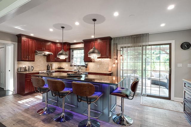 kitchen with hardwood / wood-style floors, dark stone counters, pendant lighting, a breakfast bar, and a center island