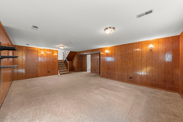 spare room featuring carpet floors, visible vents, wood walls, and stairs